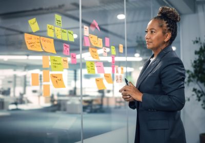 African American Businesswoman Creating Project Plan on Office Wall with Paper Notes. Stylish Confident Manager Working on Business, Financial and Marketing Projects. Specialist in Diverse Team.